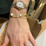 Hand wearing a gold watch with multiple bracelets and rings, blurred background