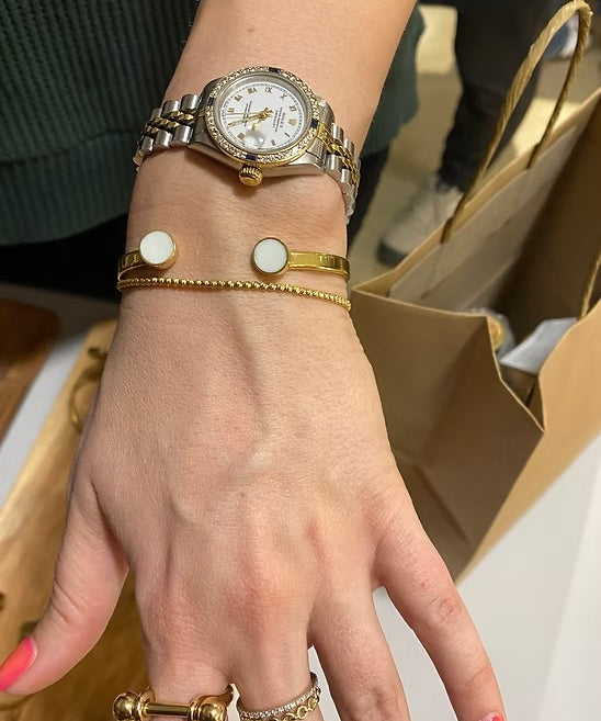 Hand wearing a gold watch with multiple bracelets and rings, blurred background