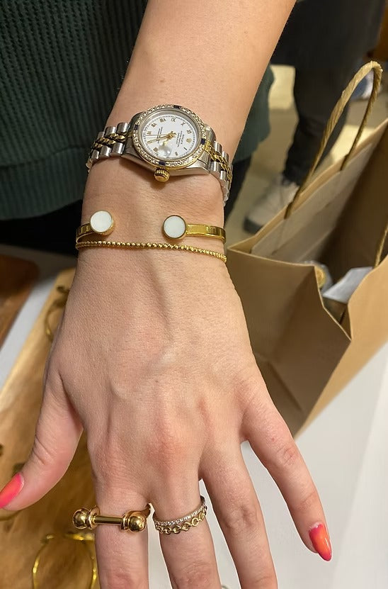 Hand wearing a gold watch with multiple bracelets and rings, blurred background